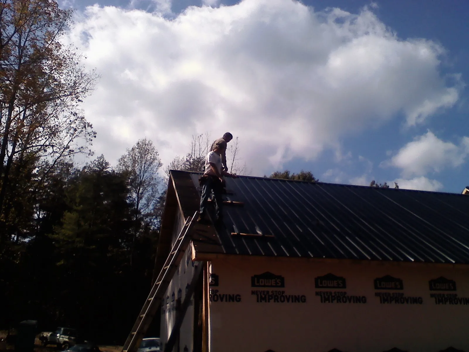 Roofer fastening dark metal panels high against a cloudy sky, from a Roof Inspection job in North Branch