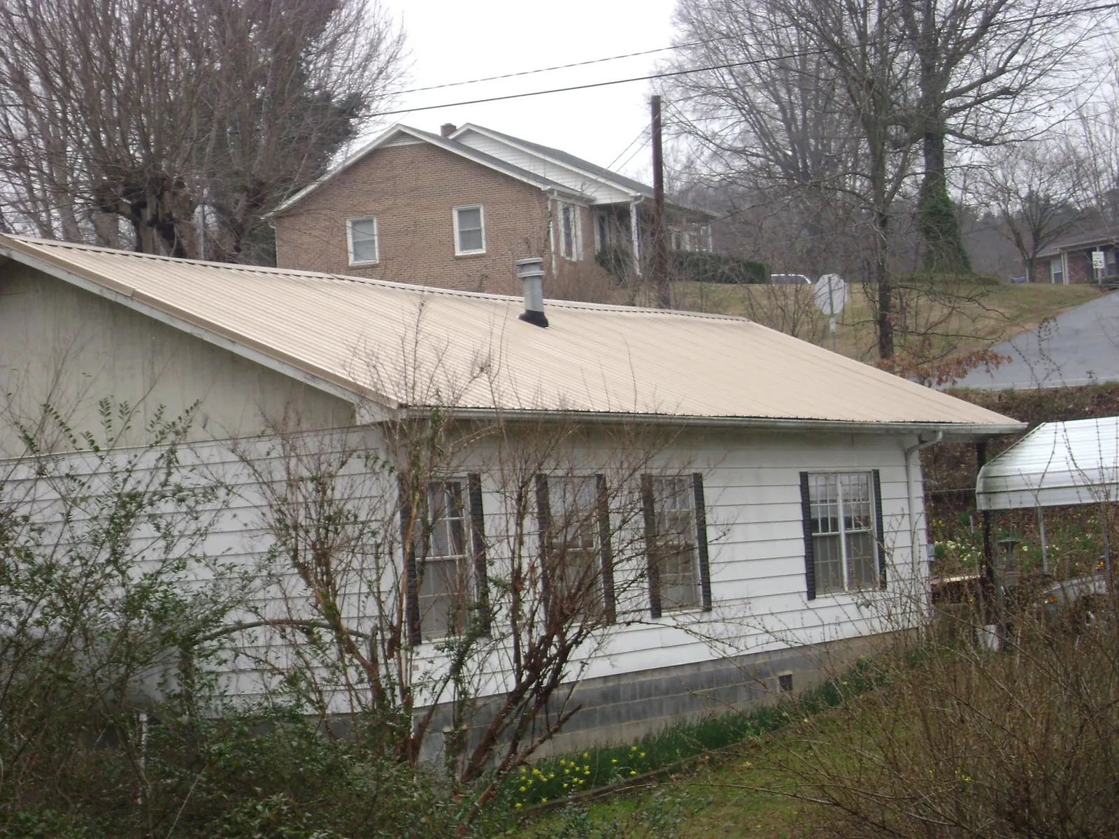 Tan metal roof on a white sided house set into a hillside — Commercial Roofing by Roofing Brothers in North Branch